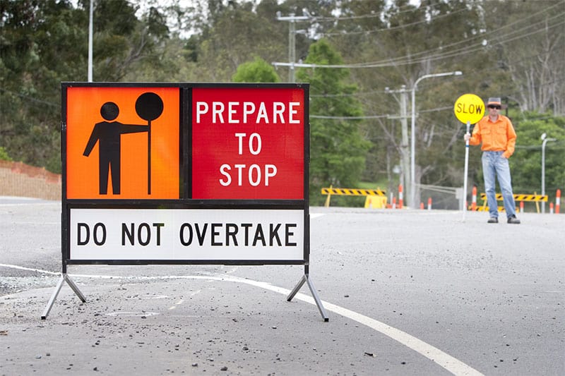 roadworks sign with employee holding slow sign